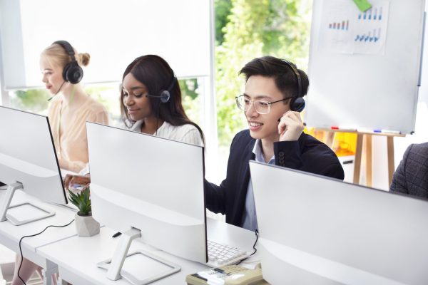 Team of helpline operators with headsets consulting clients at call center. Millennial customer service representatives working online in telemarketing at modern open space office